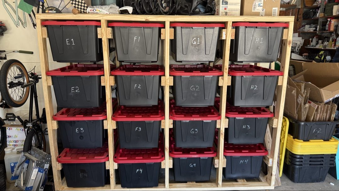 Second bin rack with storage bins labeled E1 through H4 with plywood shelf on top