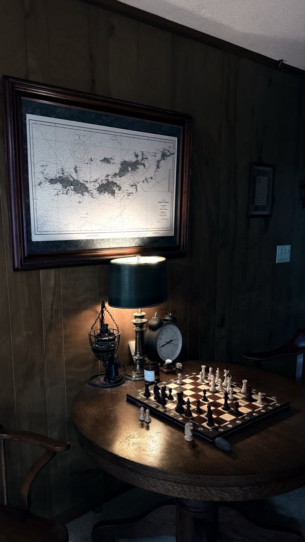 Den corner with chess set, nautical chart, antique lamp, and vintage alarm clock on round oak table