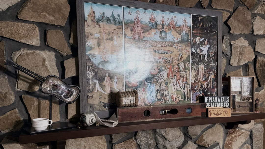 Stone fireplace mantel with framed Bosch Garden of Earthly Delights triptych, antique spirit level, vintage guitar, and collectibles
