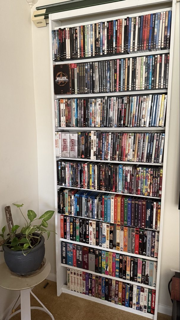 Custom floor-to-ceiling DVD and media storage rack packed with DVDs and VHS tapes